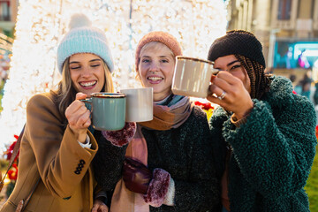 Diverse friends enjoying mulled wine at Christmas market, winter celebration, festive atmosphere
