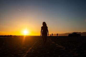 Obraz premium Woman walking on the beach at sunset with people in the distance