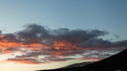 Sunset painting the clouds orange above volcanic hills in the canary islands
