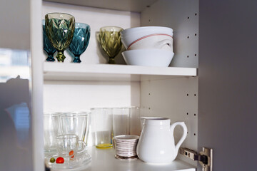 Clean dishes and tableware on white shelf