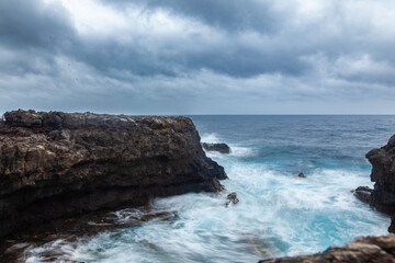 Turquoise waves crashing on rocks under stormy sky