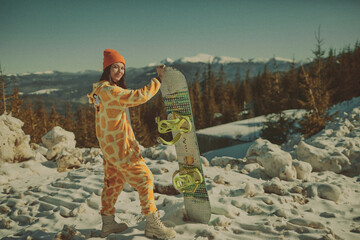  A girl with a snowboard in her hands against the backdrop of snowy mountains