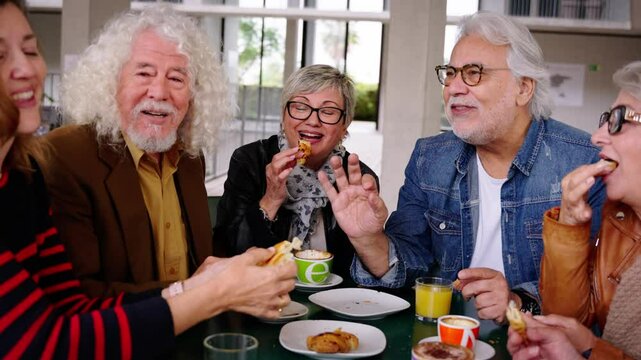 Happy senior people having breakfast sitting at cafe bar. Group of older friends having snack in restaurant chatting laughing together. Food and beverage life style on maturity concept