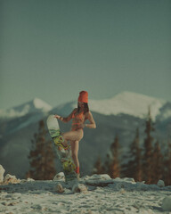  A girl with a snowboard in her hands against the backdrop of snowy mountains