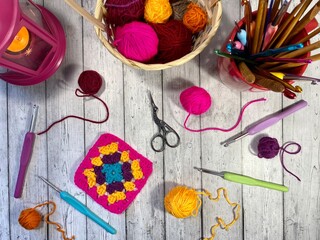 Crochet granny square, clews, hooks, scissors, basket and candle light on the table cozy home photo...