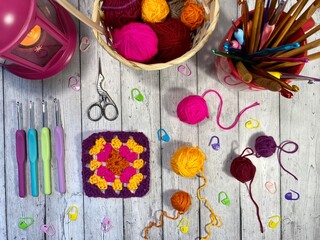 Crochet granny square, clews, hooks, scissors, basket and candle light on the table cozy home photo with hobby objects 