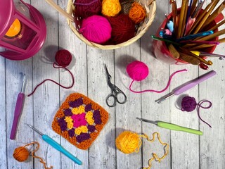 Crochet granny square, clews, hooks, scissors, basket and candle light on the table cozy home photo...
