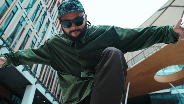 Low angle view of hipster pose in hip hop style surrounded by mall view. Portrait of sporty asian hip hop choreographer dancing break dance while looking at camera. Outdoor sport 2024. Hiphop. - Powered by Adobe