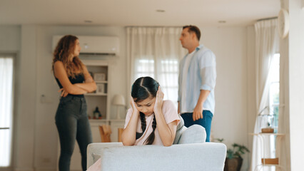 Fototapeta premium Annoyed and unhappy young girl sitting on sofa trapped in middle of tension by her parent argument in living room. Unhealthy domestic lifestyle and traumatic childhood develop to depression Synchronos