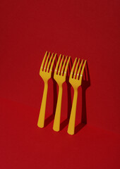 Yellow Plastic forks on red background with shadow. Minimalism. Creative layout. Food concept