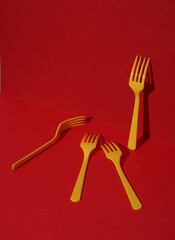 Yellow Plastic forks on red background with shadow. Minimalism. Creative layout. Food concept