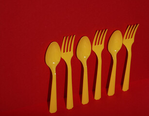 Yellow Plastic spoons and forks on red background with shadow. Minimalism. Creative layout. Food concept