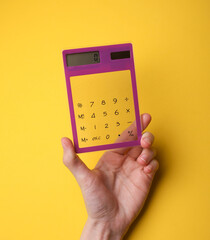 Hand holding calculator on yellow background