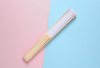 Traditional closed Asian hand fan on pink blue background