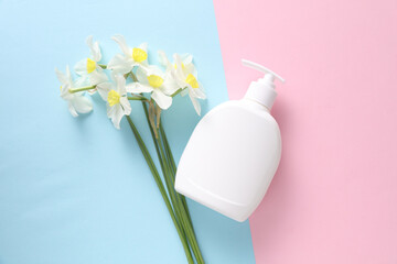 Liquid soap bottle with dispenser and flowers on blue pink background