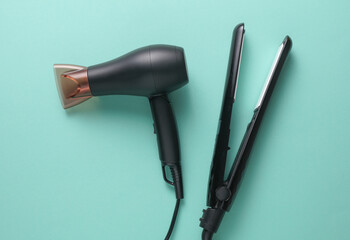 Modern black hair dryer and hair iron on blue background