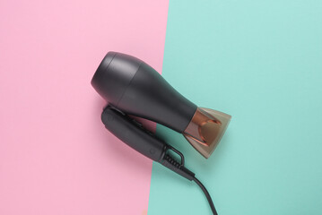 Black hair dryer on pink blue background. Top view