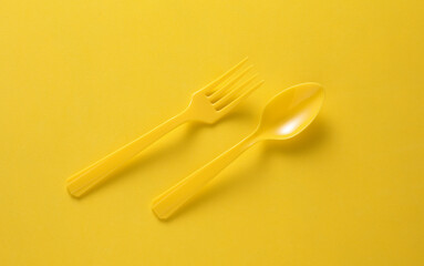 Plastic fork and spoon on yellow background