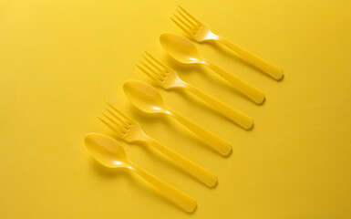 Plastic forks and spoons on yellow background