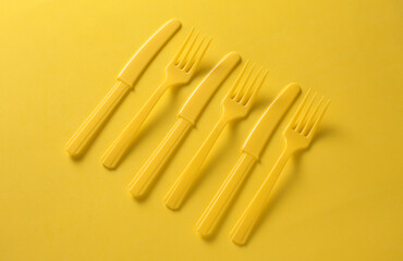 Plastic forks and knives on yellow background