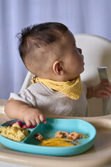 9 month old Asian baby boy is learning to eat, with food on the table, the baby eats and commands himself, it seems a bit messy