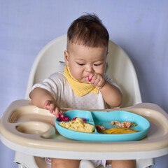 9 month old Asian baby boy is learning to eat, with food on the table, the baby eats and commands himself, it seems a bit messy