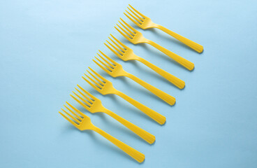 Many Yellow Plastic forks on blue background. Top view