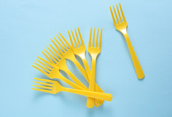 Many Yellow Plastic forks on blue background. Top view