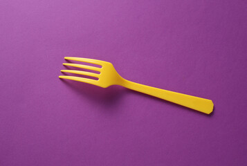 Yellow Plastic fork on purple background. Top view