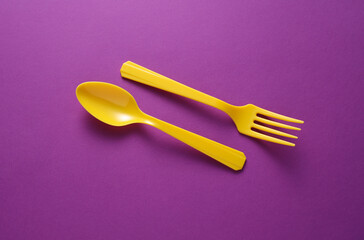 Yellow Plastic fork and spoon on purple background.
