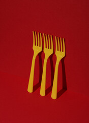Yellow Plastic forks on red background with shadow. Minimalism. Creative layout. Food concept