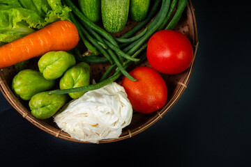 arrangement of vegetables commonly used in indonesian dishes, including tomatoes, carrot, cucumbers, long beans, pumpkin, cabbage, and lettuce. Put on traditional bamboo basket, solid black background