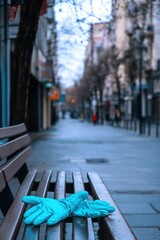 Obraz premium A pair of blue gloves rests on a bench in an empty urban street, suggesting a quiet environment.