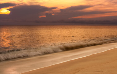 Fototapeta premium Summer sunset sky landscape,Sunrise over motion Sea ocean waves on sand beach,Beautiful golden hour in purple, orange, yellow sky by sea beach with reflections calm waves, soft sandy tropical beach