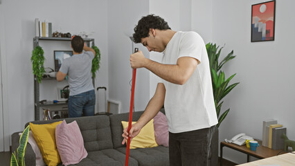 Two men cleaning the living room together, showcasing teamwork in a tidy, modern home interior.