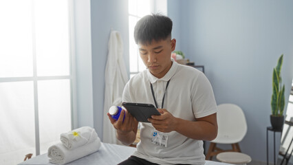 Fototapeta premium Young man in a spa wellness center holding a product bottle and using a tablet indoors, showcasing a serene and professional beauty salon environment.