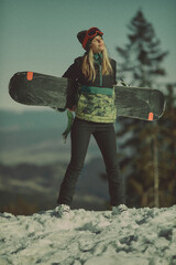 A girl with a snowboard in her hands against the backdrop of snowy mountains