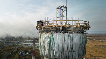 Dangerous work at height.Construction site of a power plant a high chimney.A renovation is smokestack.Contractor repairing a chimney at a highrise.Workers in a hard hat.Dangerous work at the high site