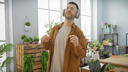Handsome young man dancing with headphones in a vibrant indoor flower shop