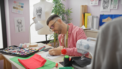 Hispanic man sketching in a colorful tailor shop with sewing machine and fabric, focusing on...