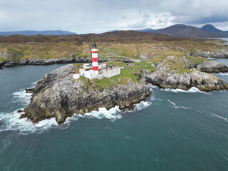 Looking out across the Minch to the Isle of Skye, the red and white Eilean Glas Lighthouse on the east coast of the island of Scalpay in the Outer Hebrides, Scotland, UK