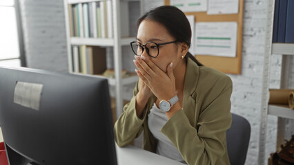 Woman in office surprised by news on computer screen, wearing glasses and blazer in a modern workplace setting in china