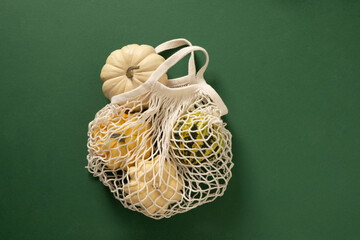 Autumn white decorative small pumpkins in mesh shopping bag on green background. Harvest day...