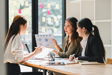 Collaborative business meeting with three women discussing charts and graphs, showcasing teamwork and professional engagement in modern office setting