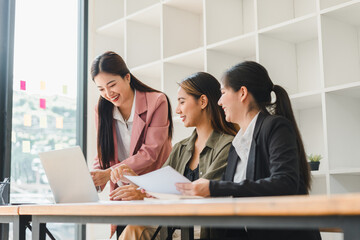 Collaborative women working together in modern office, discussing ideas and reviewing documents while using laptop. Their expressions reflect enthusiasm and teamwork