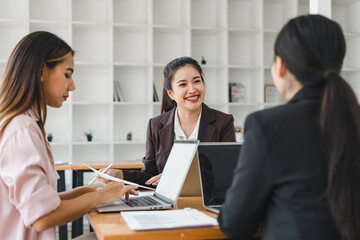 Fototapeta premium Professional women engaged in collaborative meeting, discussing ideas and strategies with laptops and documents on table. Their expressions reflect enthusiasm and teamwork