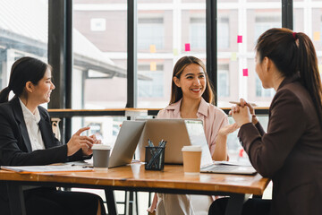 Collaborative business meeting with three women discussing ideas at modern office table. They are engaged and smiling, showcasing teamwork and communication