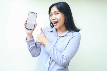 Fototapeta premium pretty smiling asian young business woman holding mobile phone with empty screen giving thumbs up, approval and good sign gesture, show app and product wear formal shirt isolated on white background