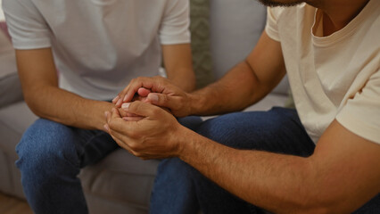 Father and son sit together in a living room, sharing a heartfelt moment of love and support, holding hands, highlighting their family bond and connection at home.