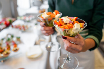 Close-up of hands holding a glass bowl filled with fresh salad at a social gathering, showcasing healthy eating. The vibrant mix of vegetables highlights a nutritious and colorful meal option.